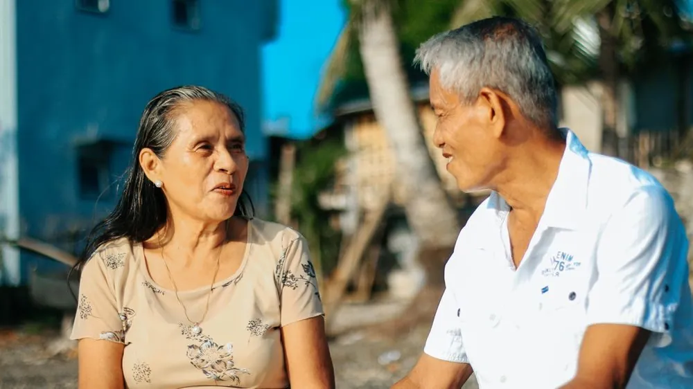 Elderly couple sitting outside, sharing a joyful moment together in a sunny setting.