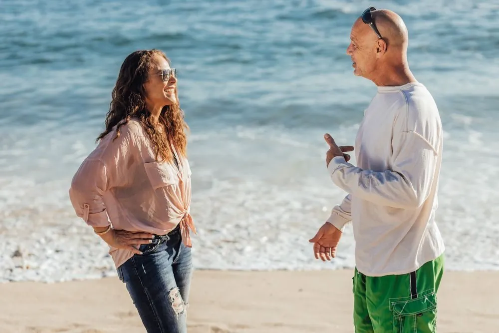 Elderly couple shares a joyful conversation by the shore on a sunny day.
