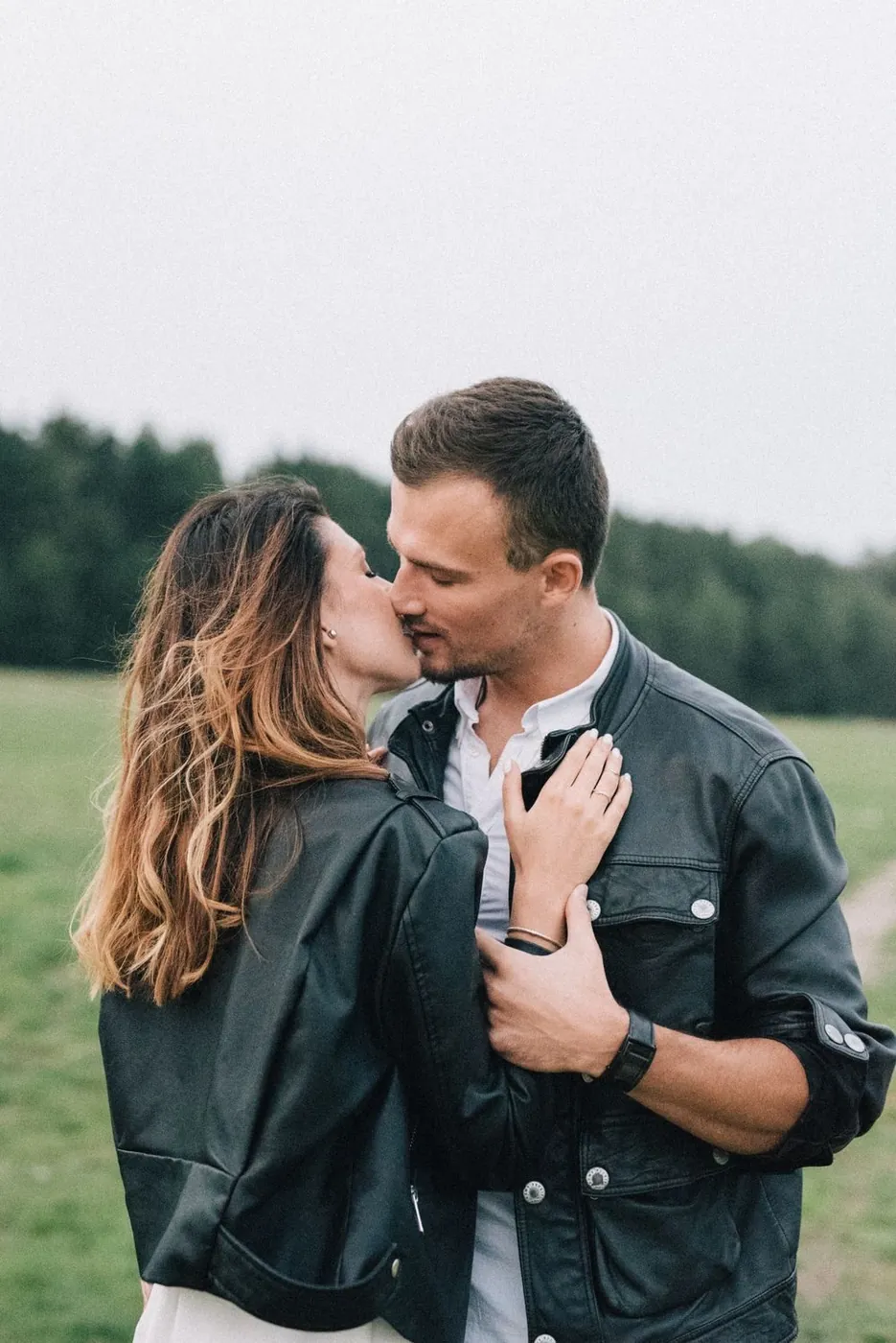 A couple sharing a romantic kiss outdoors, dressed in stylish black leather jackets.