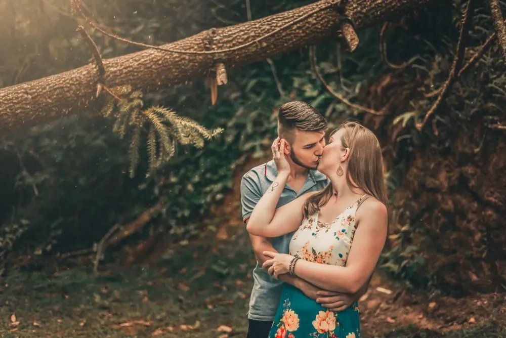 A couple shares a romantic kiss surrounded by lush forest scenery, adding a touch of nature and intimacy.