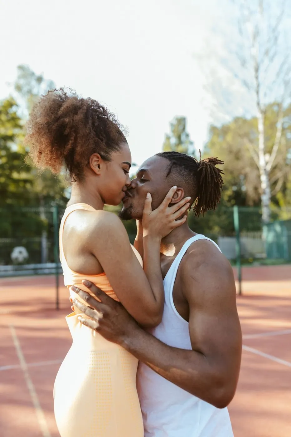 Loving couple sharing a kiss on a sunny tennis court. Outdoor romance.