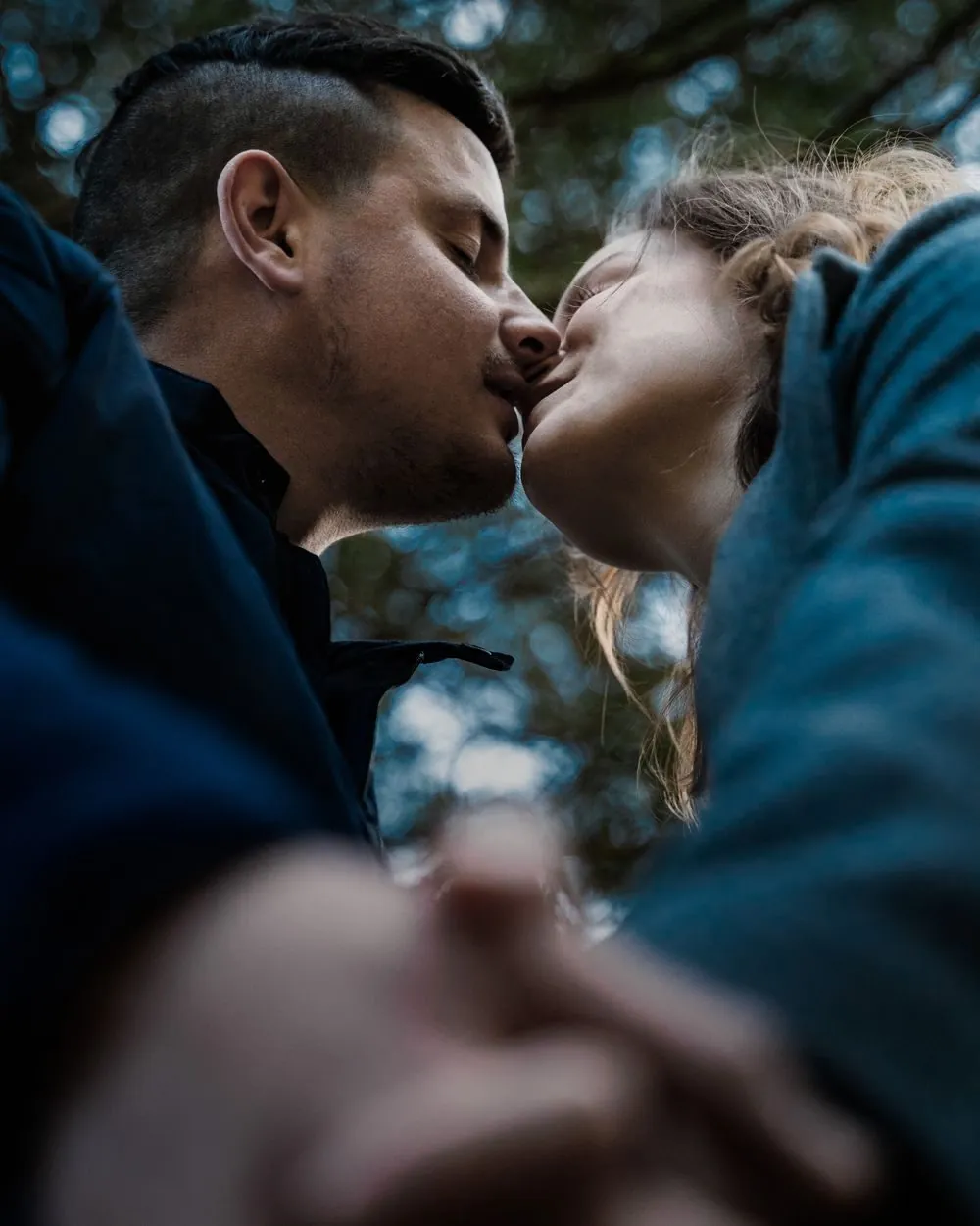 Low-angle shot of a couple kissing, showcasing affection and romance with a blurred natural background.