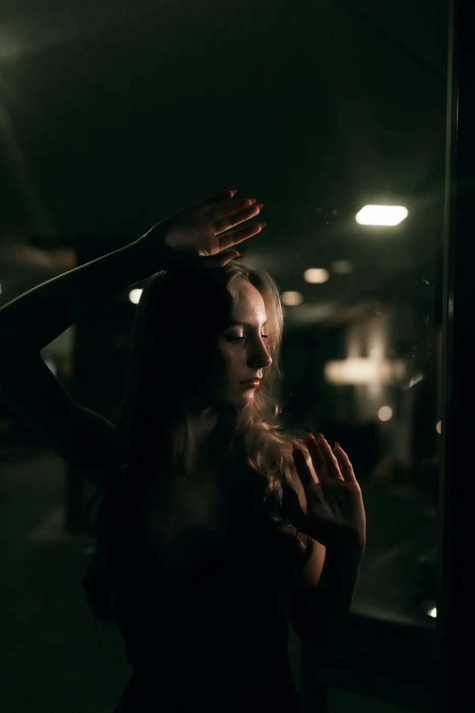 A dramatic, moody portrait of a woman in a dimly lit urban setting at night.