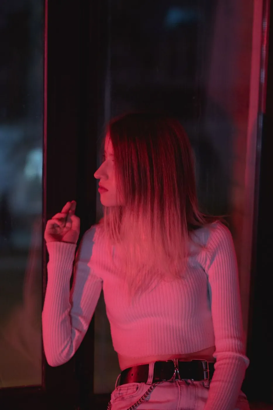 A young woman sitting by a window, illuminated by moody red lighting.