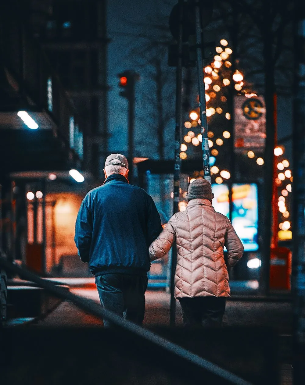 Couple walking arm in arm on a city street at night, dressed in winter clothes with bokeh lights.