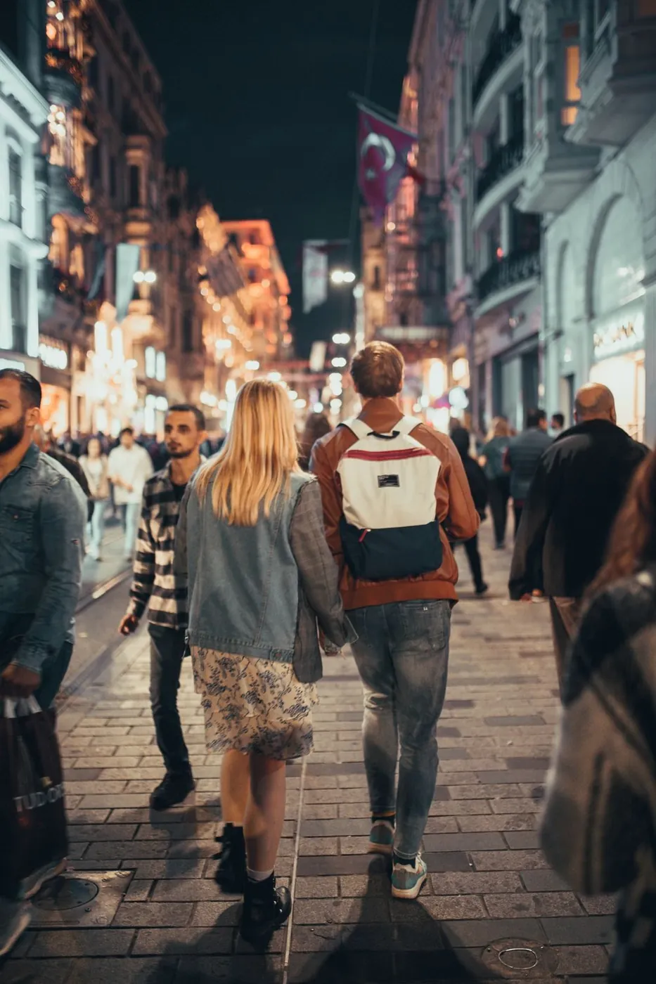 Couple walking hand in hand on a lively city street at night, capturing urban life.