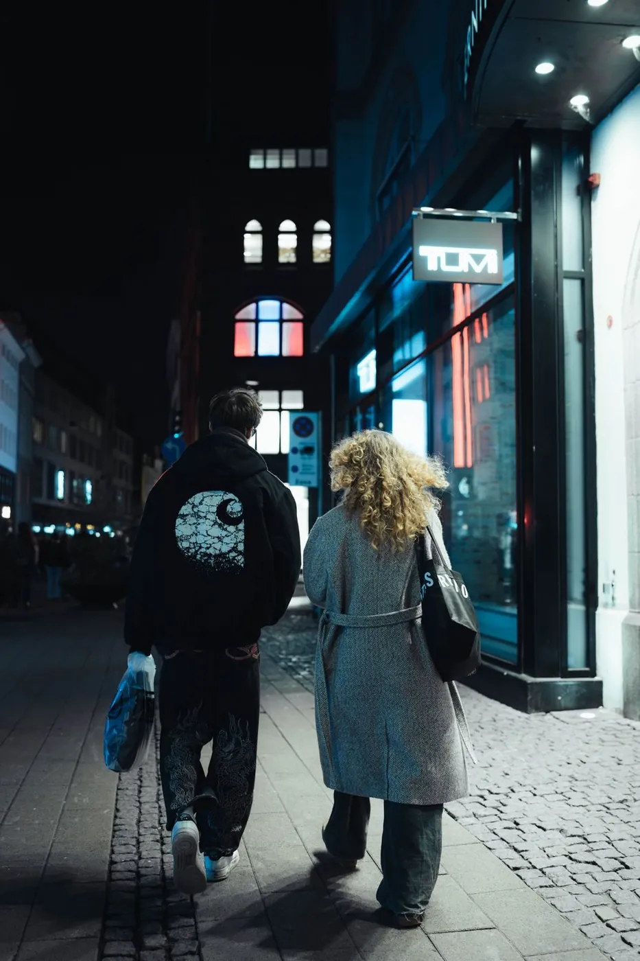 Couple strolling at night in a vibrant city street under neon lights.