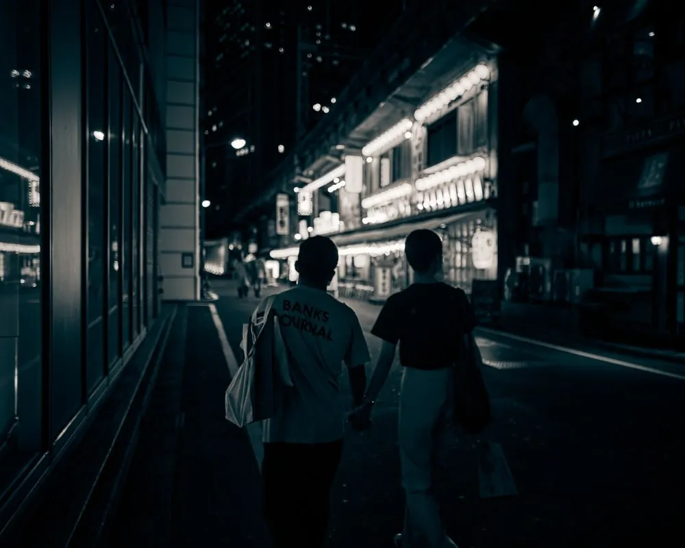 A couple walking along a bright, neon-lit street at night, holding hands and enjoying the city ambiance.